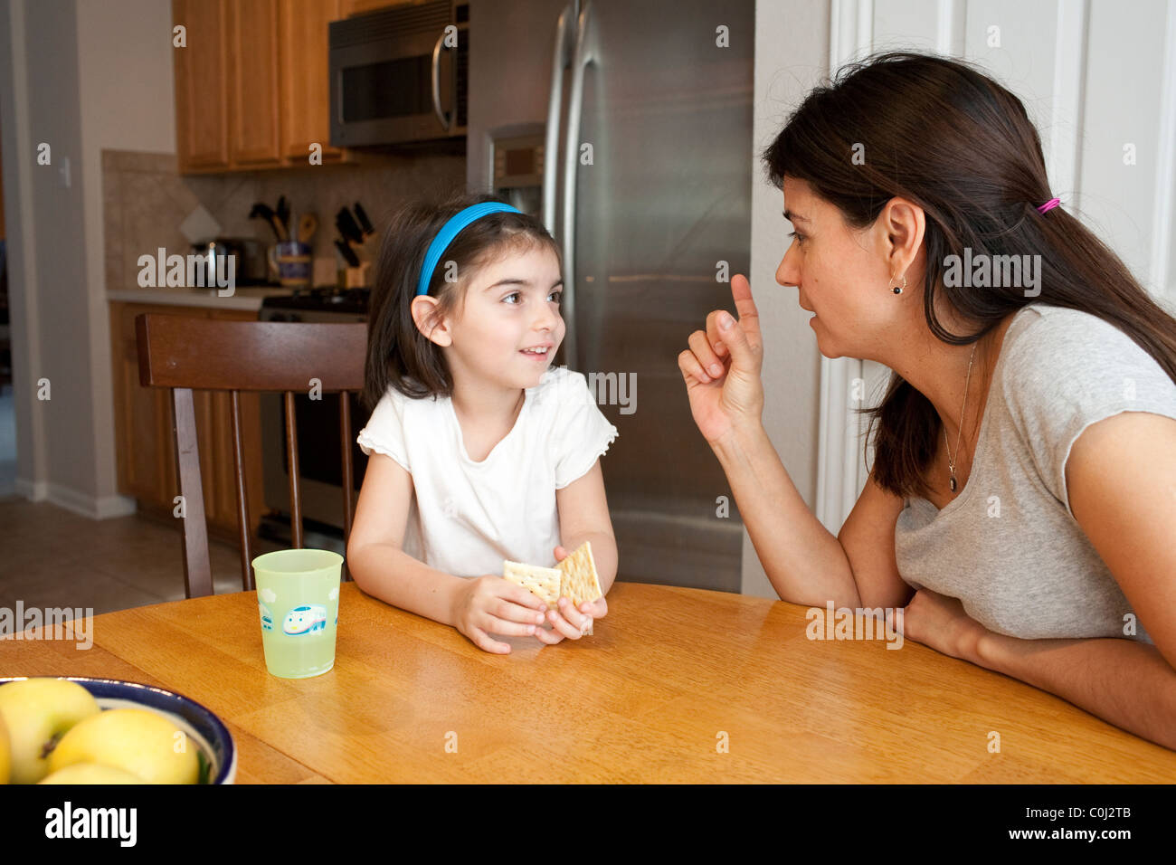 Hispanic mother makes a point to her five-year-old daughter at breakfast room table in their home in Austin Texas Stock Photo