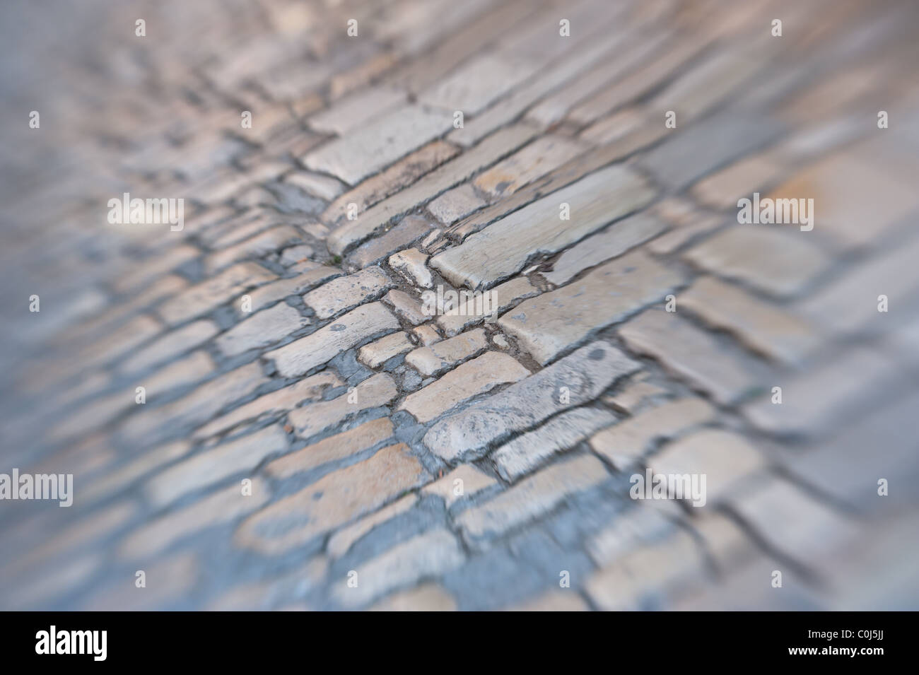 Old Roman stone pavement background, sharp in the middle and blurred to the edges. Tilt-shift lens shot. Stock Photo