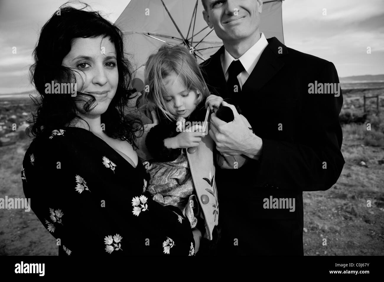 Family of three posing for a family portrait in the desert landscape with a green umbrella. Stock Photo