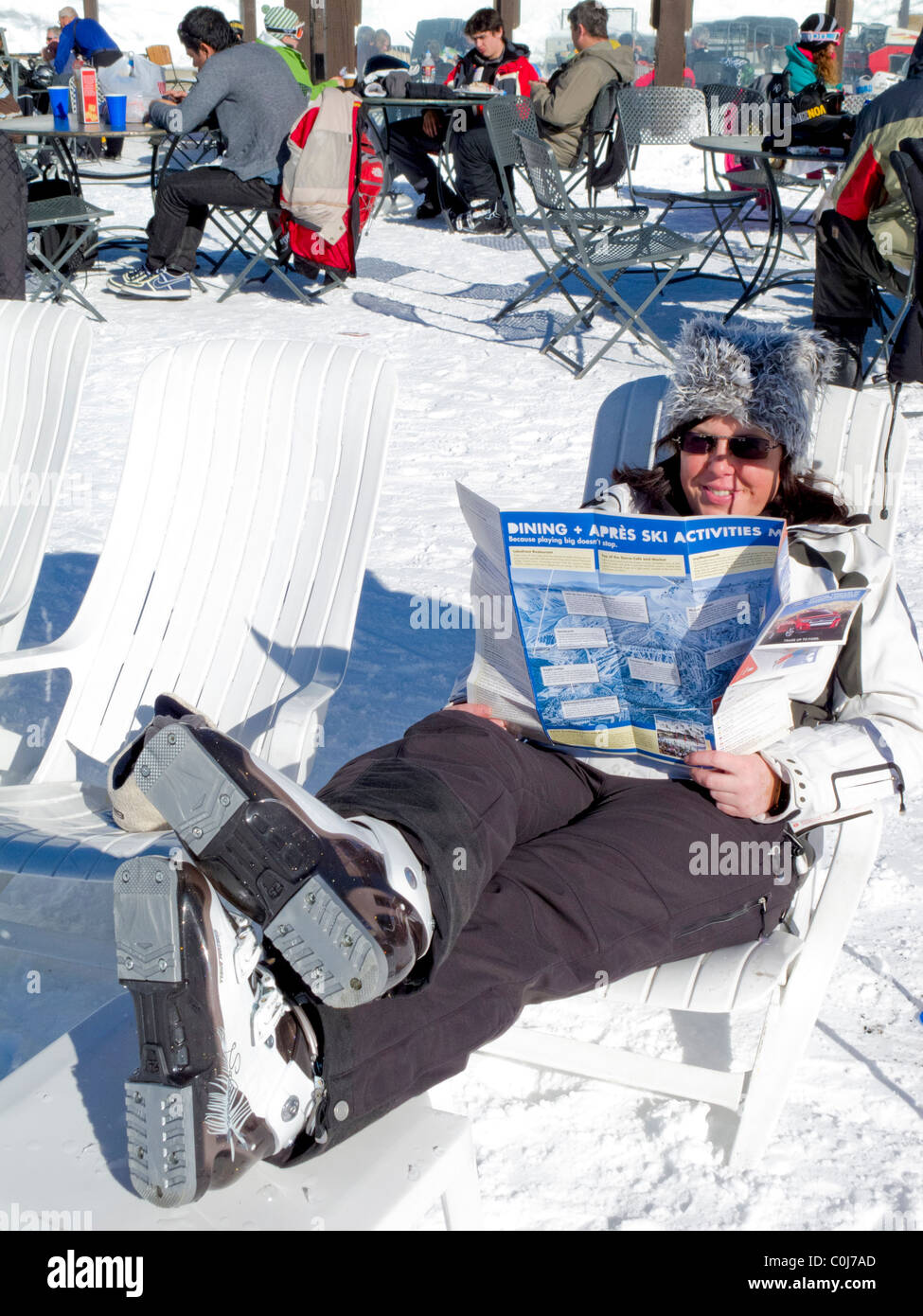 Skier reads her ski trail map and relaxes on a beach chair onslop at Mammoth Mountain ski resort, California, USA Stock Photo