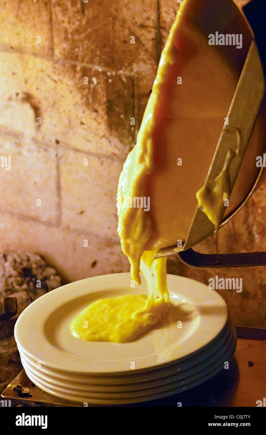 Wheel of raclette cheese melting before fireplace Stock Photo