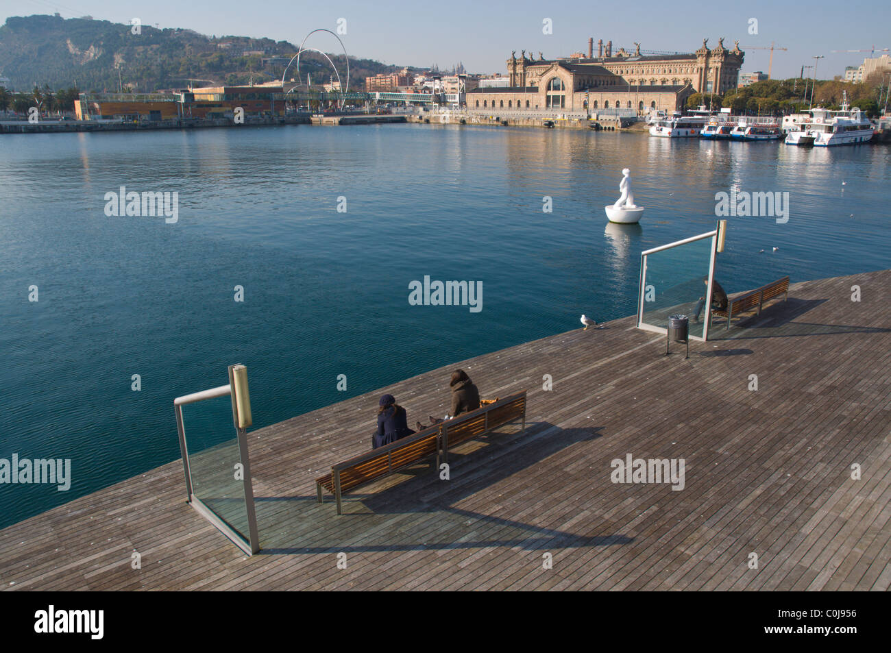 People sitting on benches at Rambla del Mar footpath at Port Vell central Barcelona Catalunya Spain Europe Stock Photo