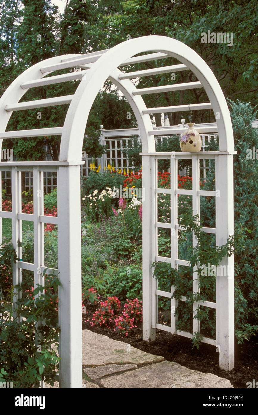 CLIMBING ROSE ON NEW GARDEN ARBOR. CATMINT AND BEGONIAS LINE STONE WALK.  MINNESOTA. Stock Photo