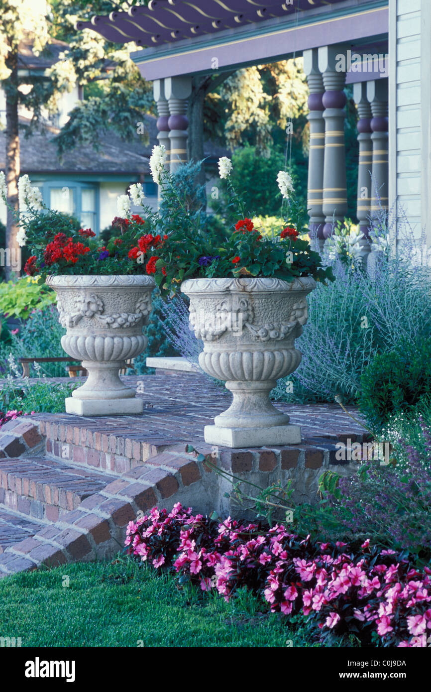 GARDEN URNS FILLED WITH ANNUALS ON STEPS OF VICTORIAN-STYLE AMERICAN HOME.  SUMMER. Stock Photo