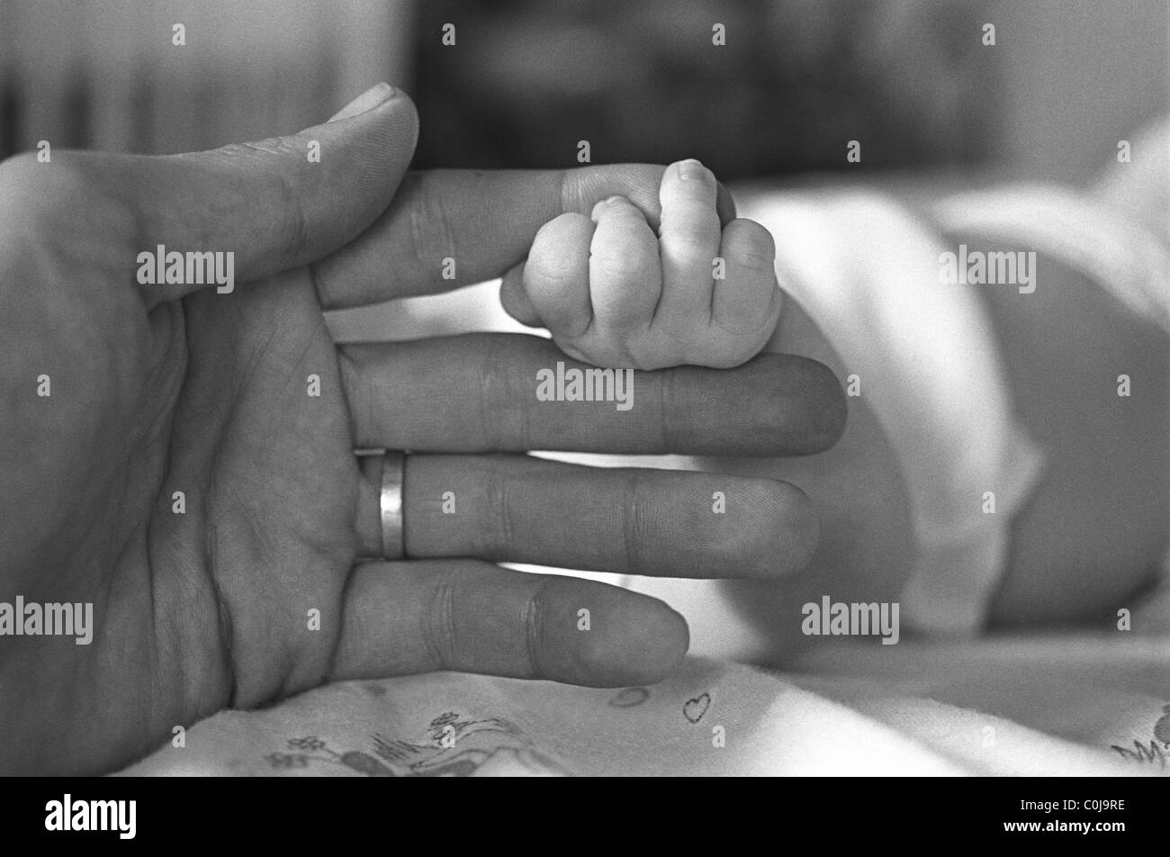 Infant holding father's finger. Stock Photo