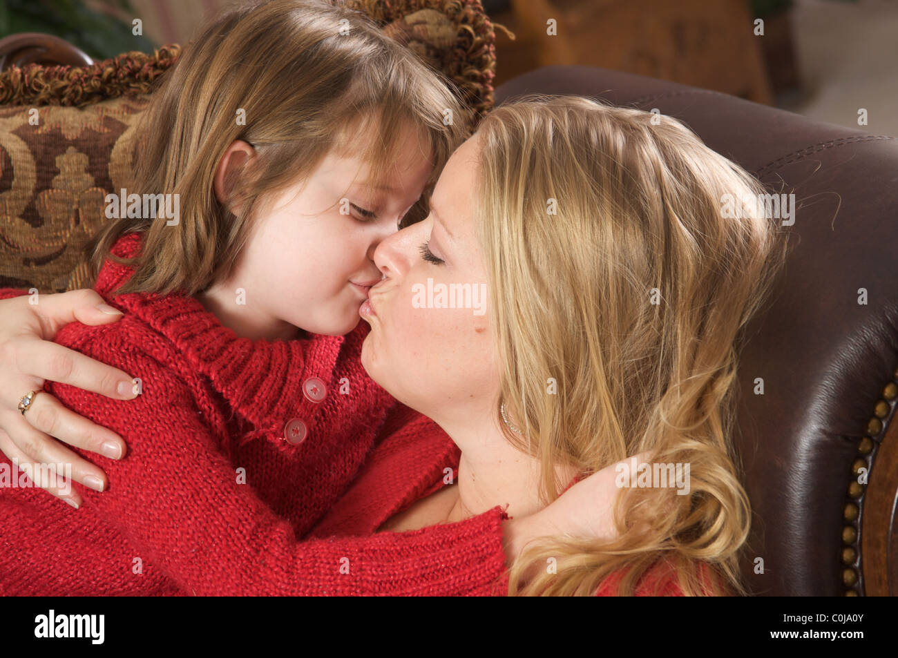 A mother smiles as she receives a kiss on the cheek from her young daughter...