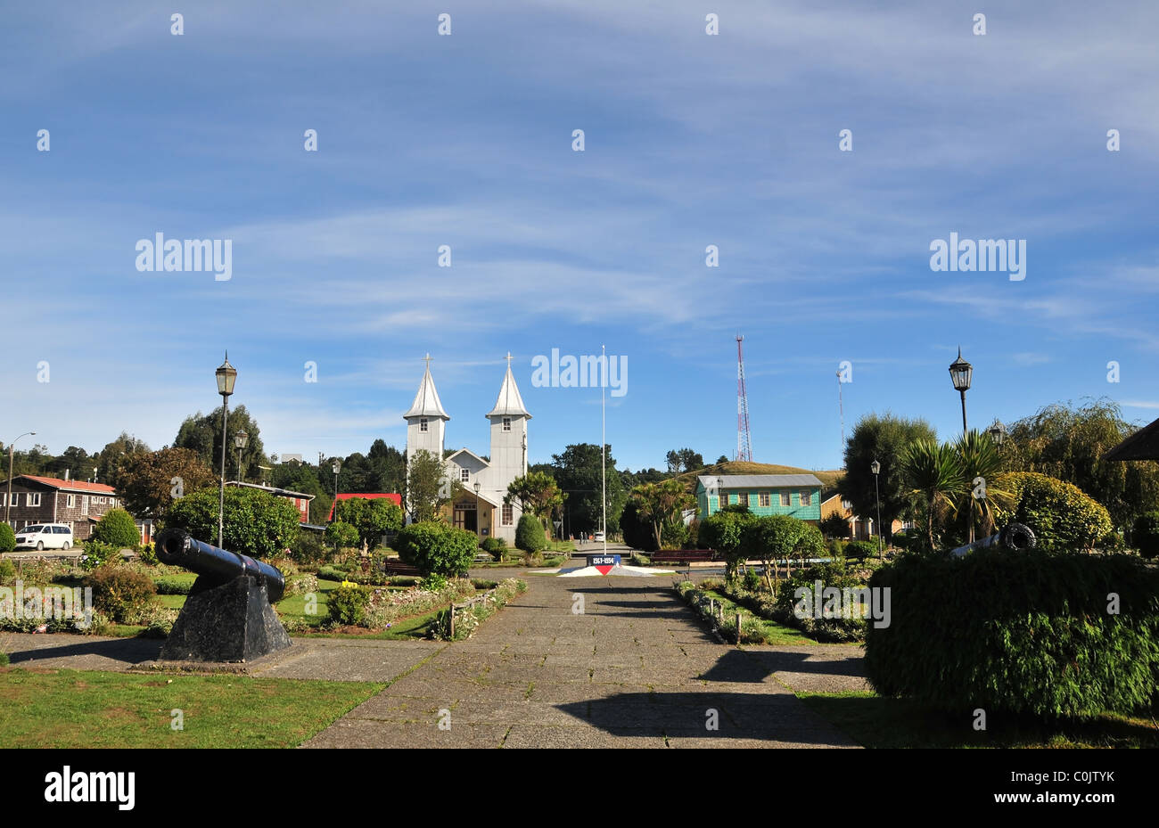Blue sky view of silver metal church, black cannon and green garden plots, Plaza Martin Ruiz, Chacao, Chiloe Island, Chile Stock Photo