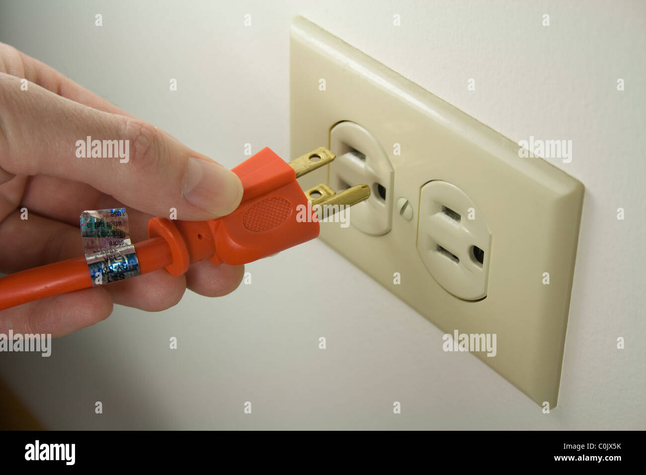 Hand Plugging Power Cord into Wall Outlet - Electrical Stock Photo