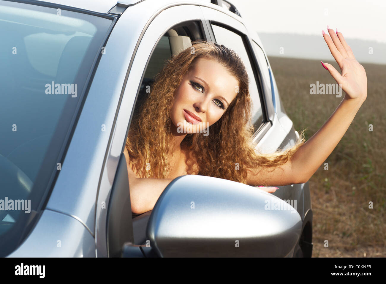 Young woman looking out of car and waving hand. Stock Photo
