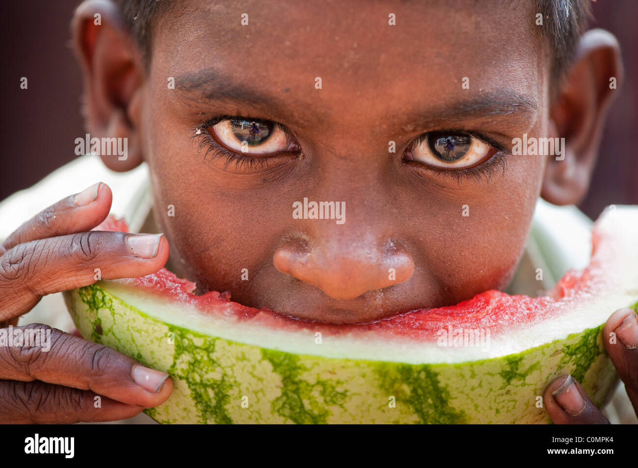 Happy young poor lower caste Indian street boy eating a slice of watermelon. Close up selective focus Stock Photo