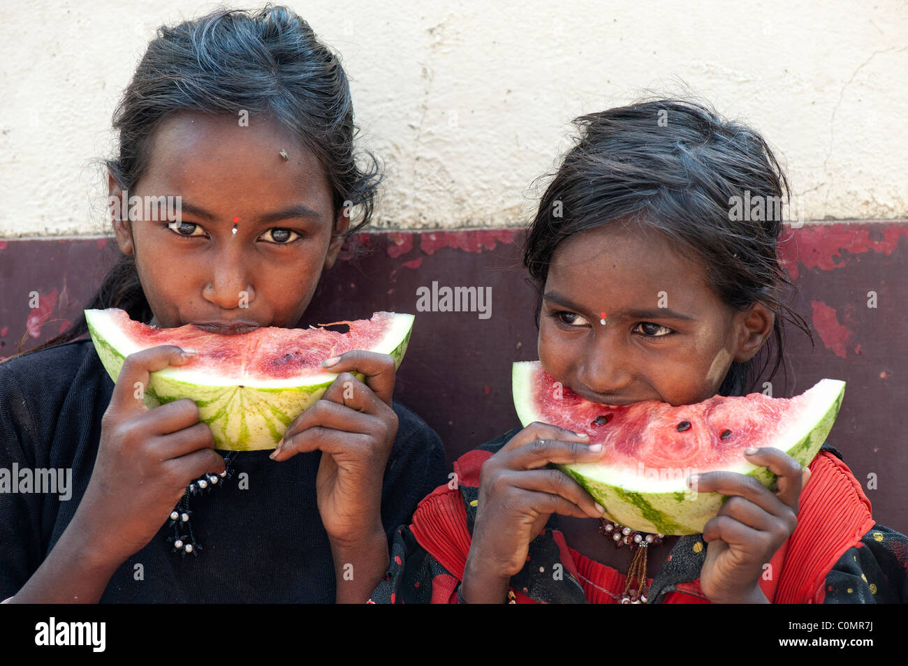 Happy young poor lower caste Indian street girls (sisters) eating a slice of watermelon. Andhra Pradesh, India Stock Photo