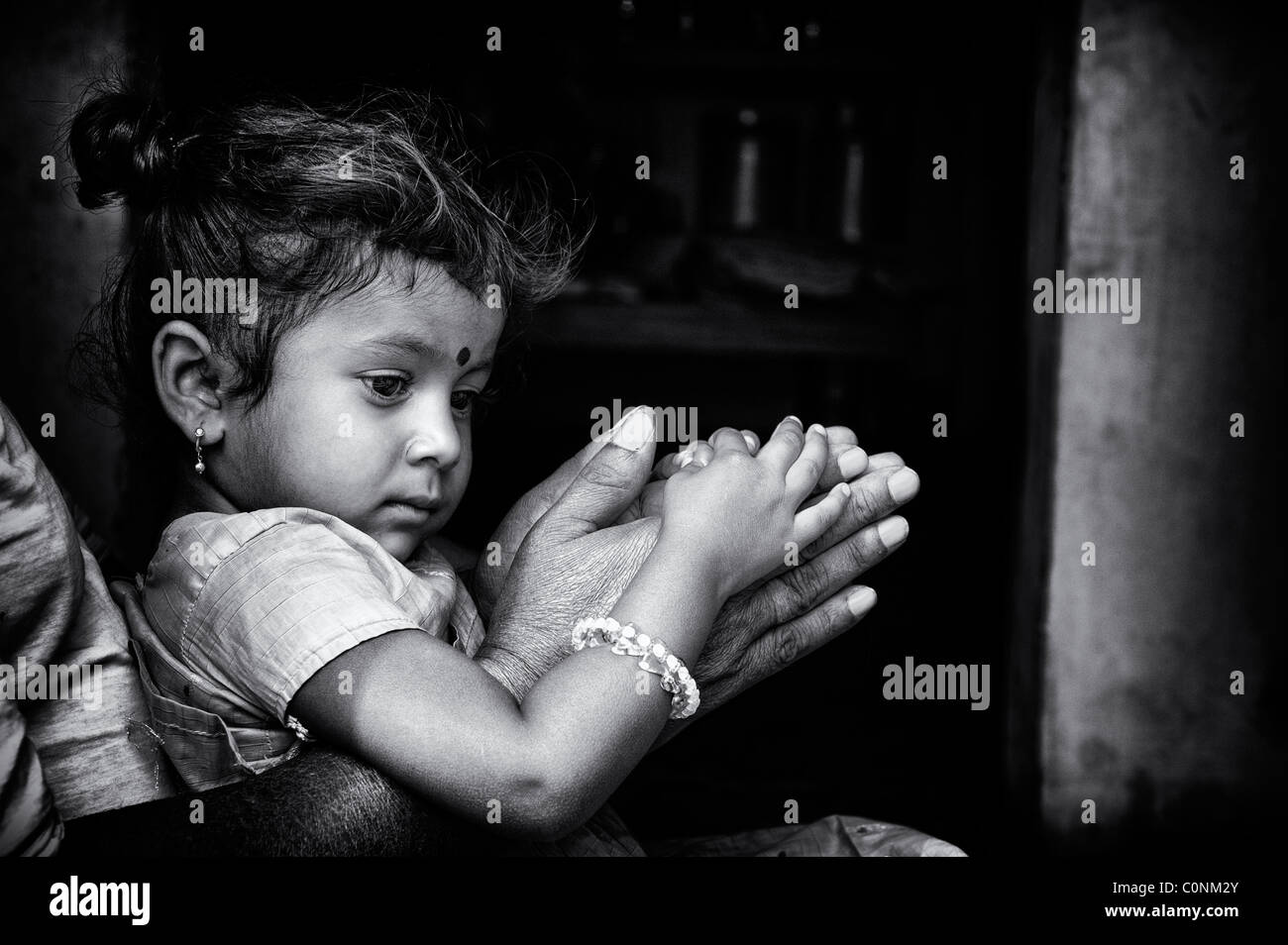 Indian girl sitting on grandads lap resting on prayer hands. Andhra Pradesh, India. Black and white. Stock Photo