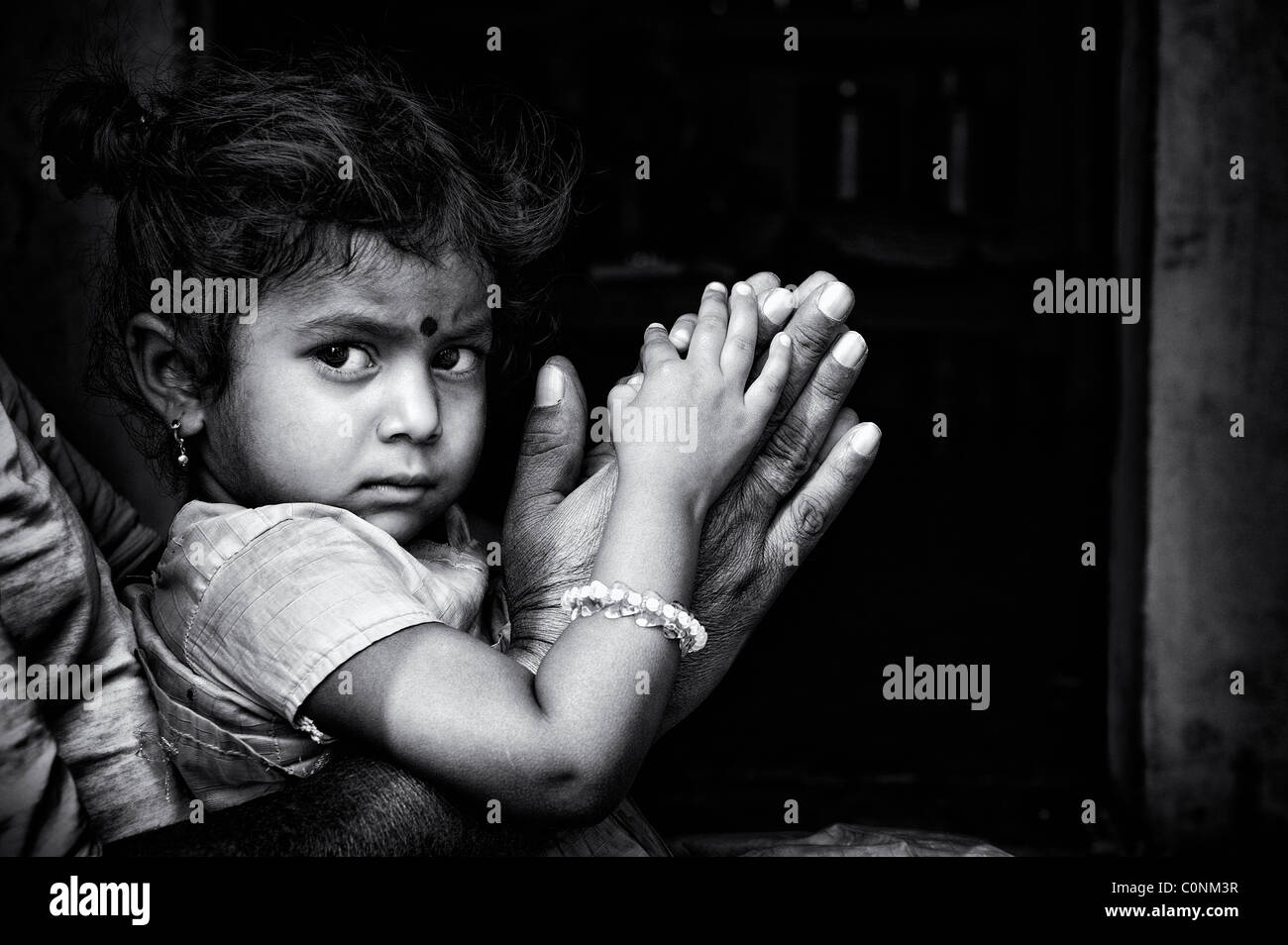 Indian girl sitting on grandads lap resting on prayer hands. Andhra Pradesh, India. Black and white. Stock Photo