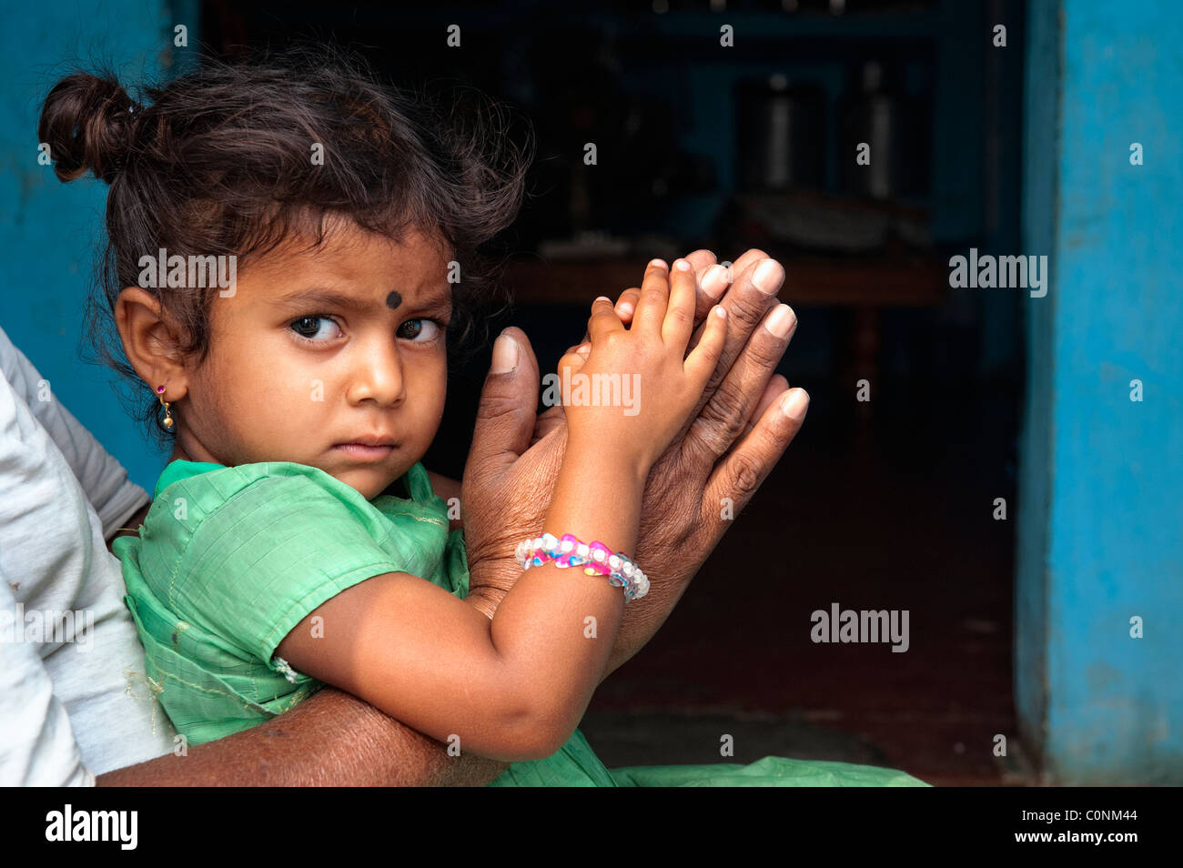 Indian girl sitting on grandads lap resting on prayer hands. Andhra Pradesh, India Stock Photo