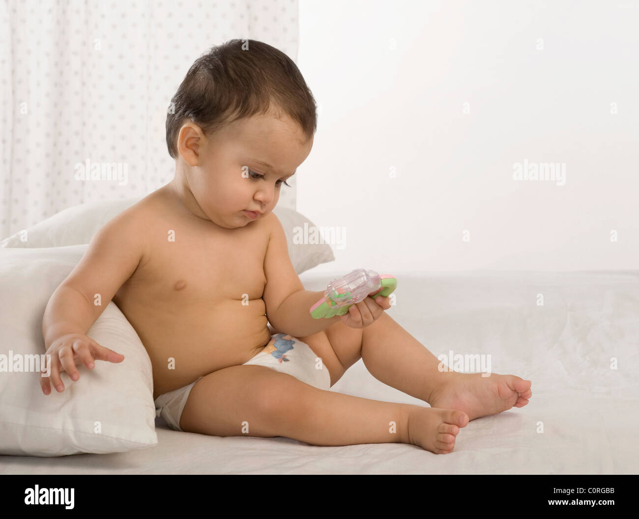 Baby boy playing with a rattle on the bed Stock Photo