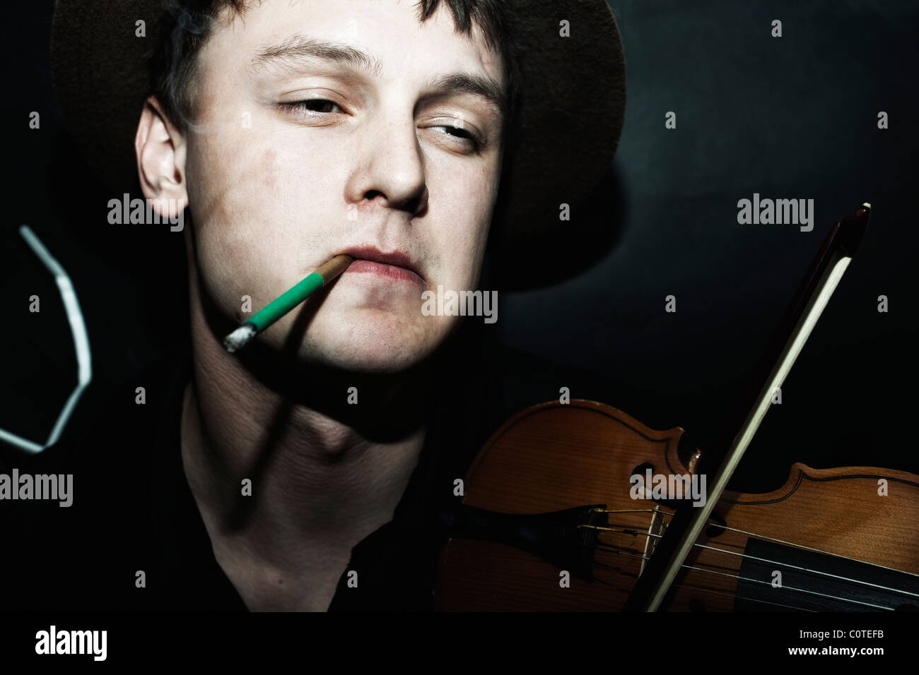 young handsome guy in hat with cigarette, playing the violin Stock Photo