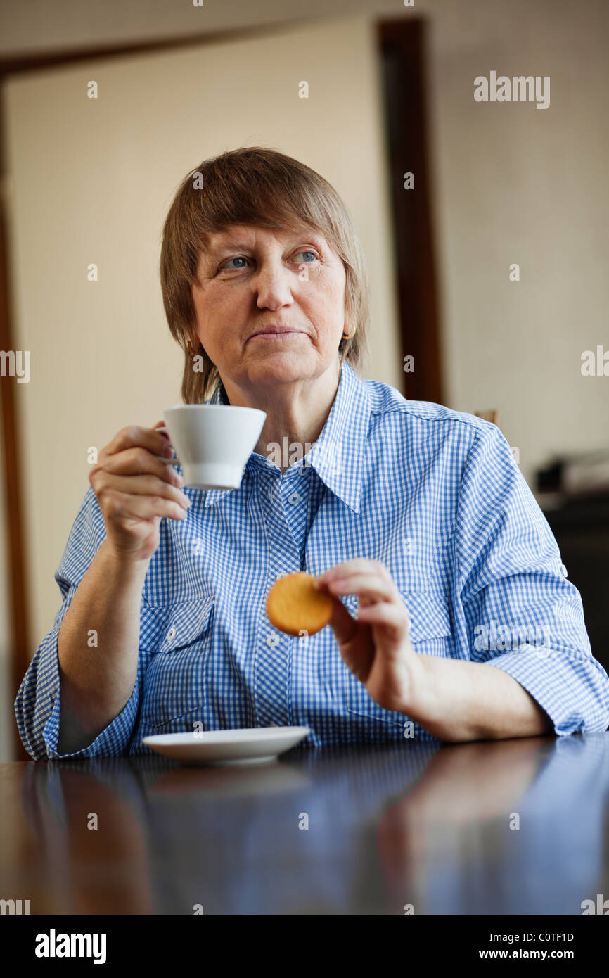 Senior woman enjoying a cup of coffee and cookie at home Stock Photo