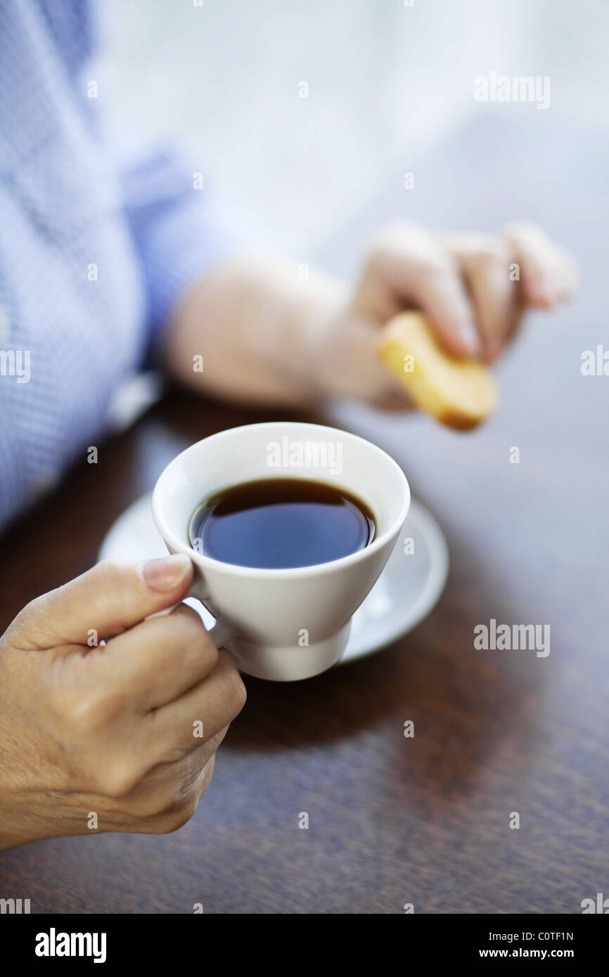 Hands of an elderly woman holding cup of coffee and cookie Stock Photo