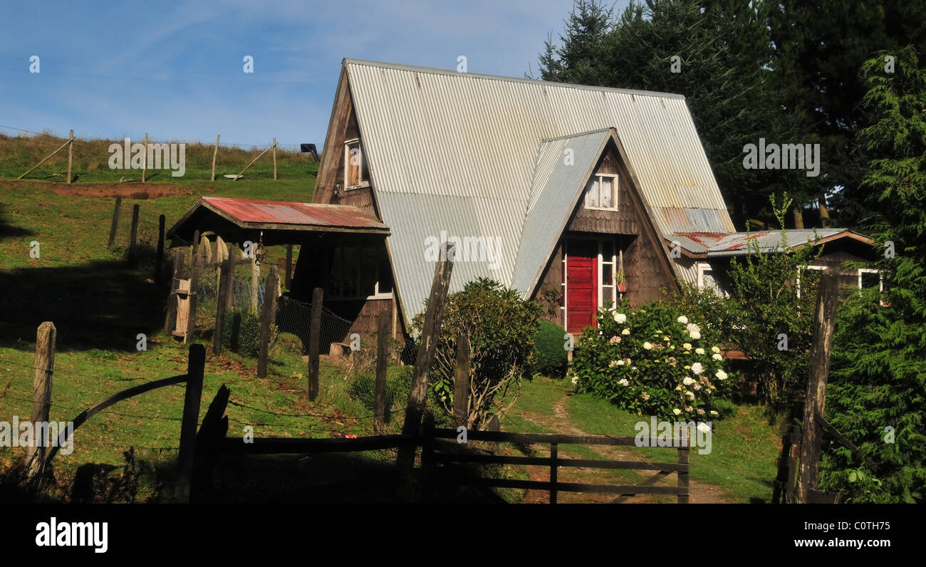 Rural roadside view of a Chilean-German house with high pitched metal roof and wood shingle walls, Caulin, Chiloe island, Chile Stock Photo