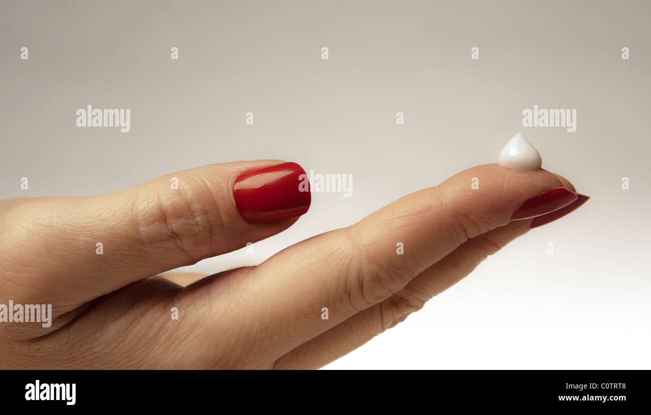 close up detail image of womans hand with red nails and a drop of hand cream Stock Photo