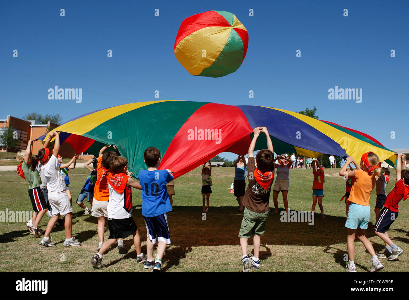 Elementary students use colorful striped tarp or parachute to bounce