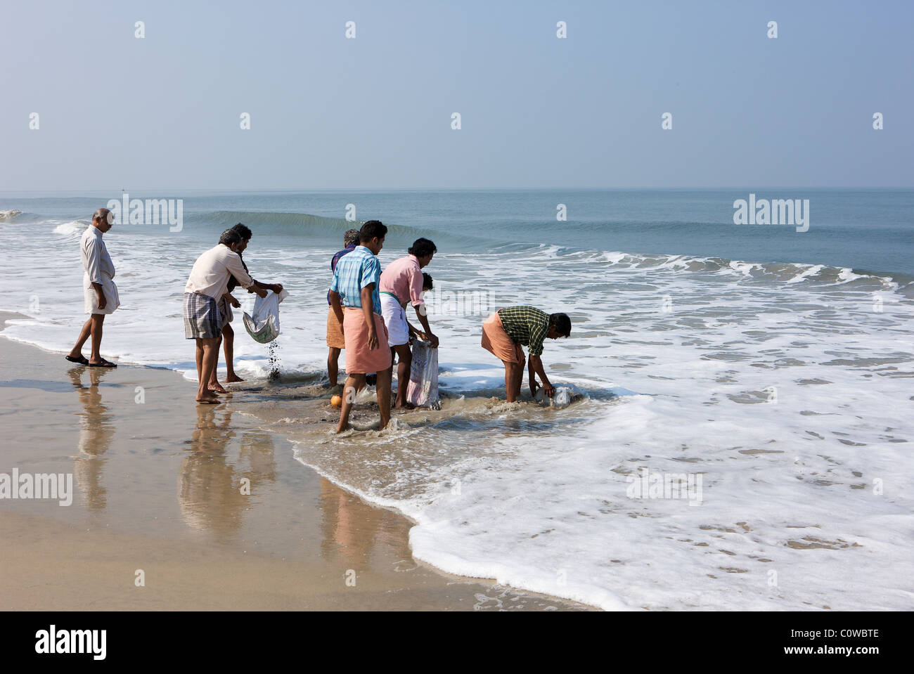 Keralite men consign the remains of a funeral pyre to the Arabian sea south of Kochi, Kerala, India Stock Photo