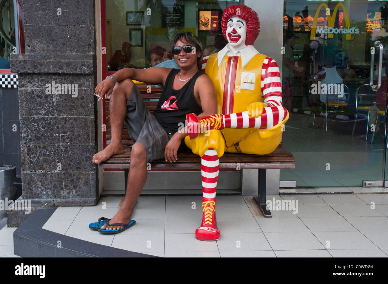 A Balinese man sitting with the Ronald McDonald clown outside the Sanur Beach branch of McDonalds in Bali Indonesia Stock Photo