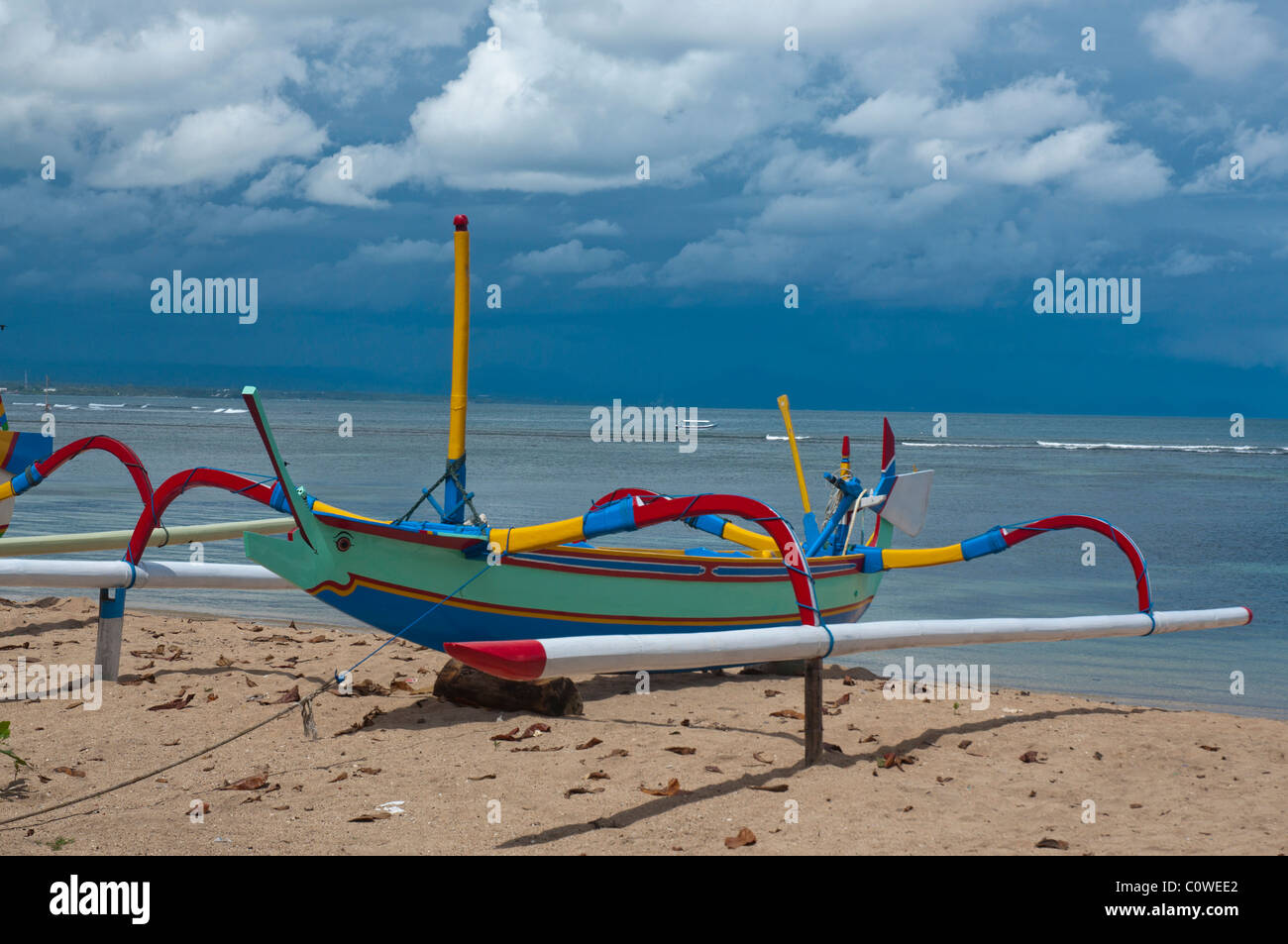 Colorful Balinese fishing boat called jukung in sunlight against a monsoon sky on Sanur Beach, Bali Indonesia  Stock Photo