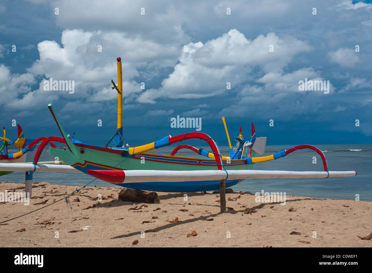 Colorful Balinese fishing boat called jukung in sunlight against a monsoon sky on Sanur Beach, Bali Indonesia  Stock Photo