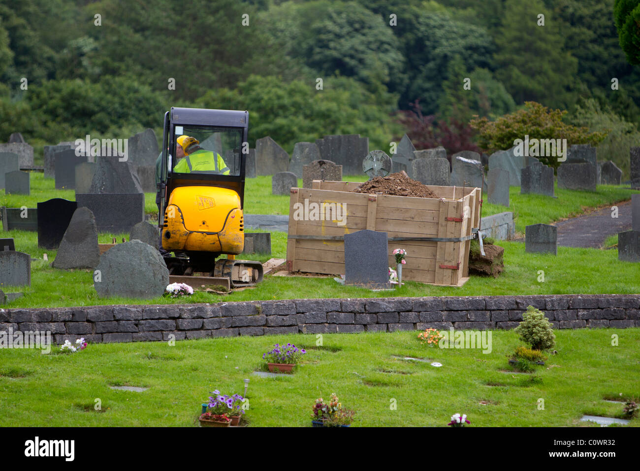 Digging grave with mechanical digger Mini JCB in grave yard Stock Photo