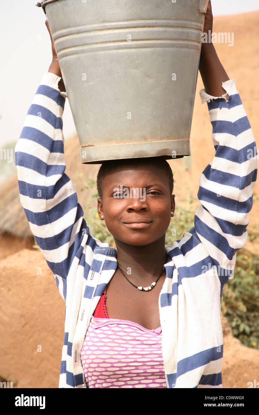 A young girl carries a bucket of water on her head after collecting it