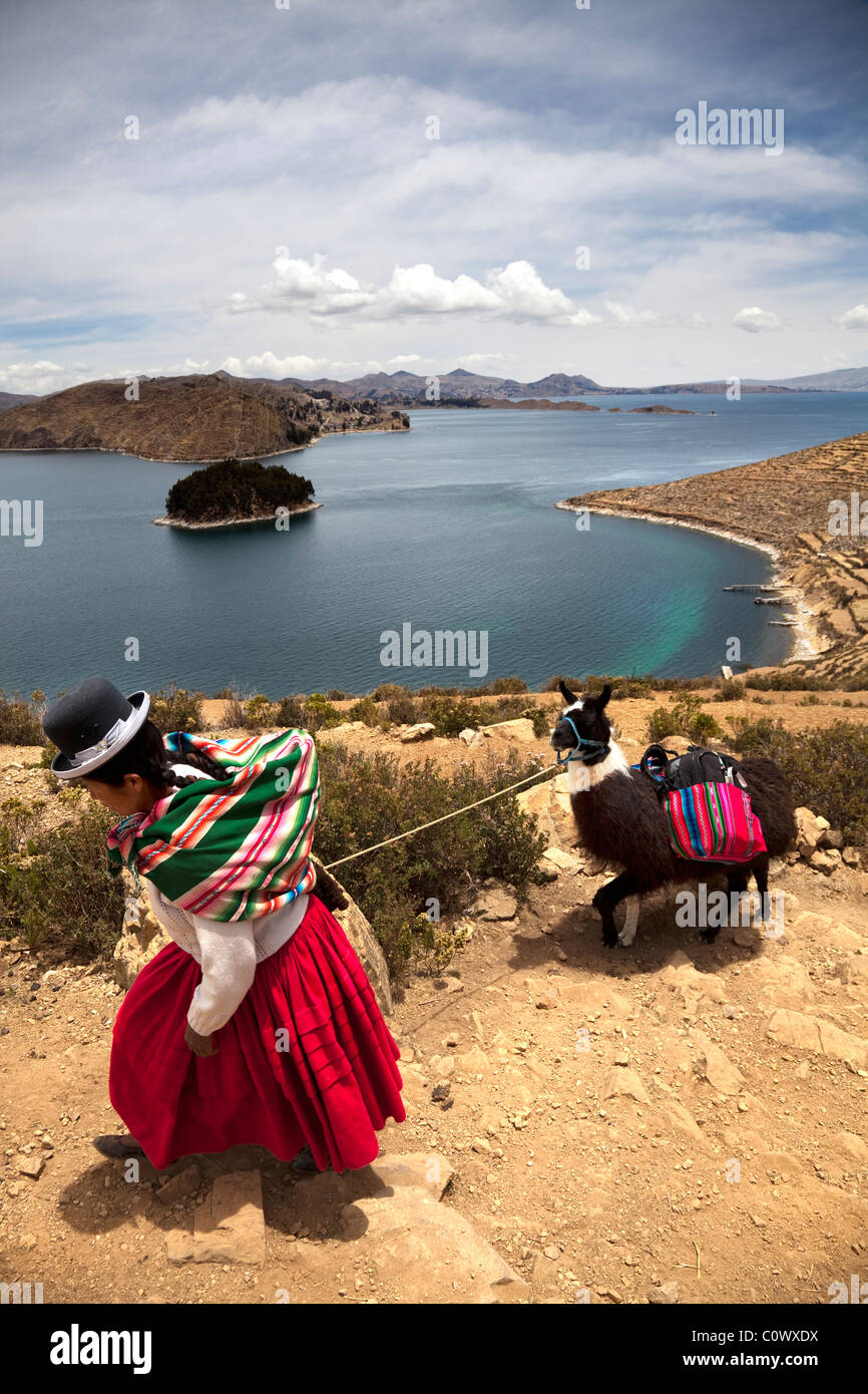 Lady in traditional Bolivian dress leading a Llama with views of Lake Titicaca, Bolivia, South America. Stock Photo