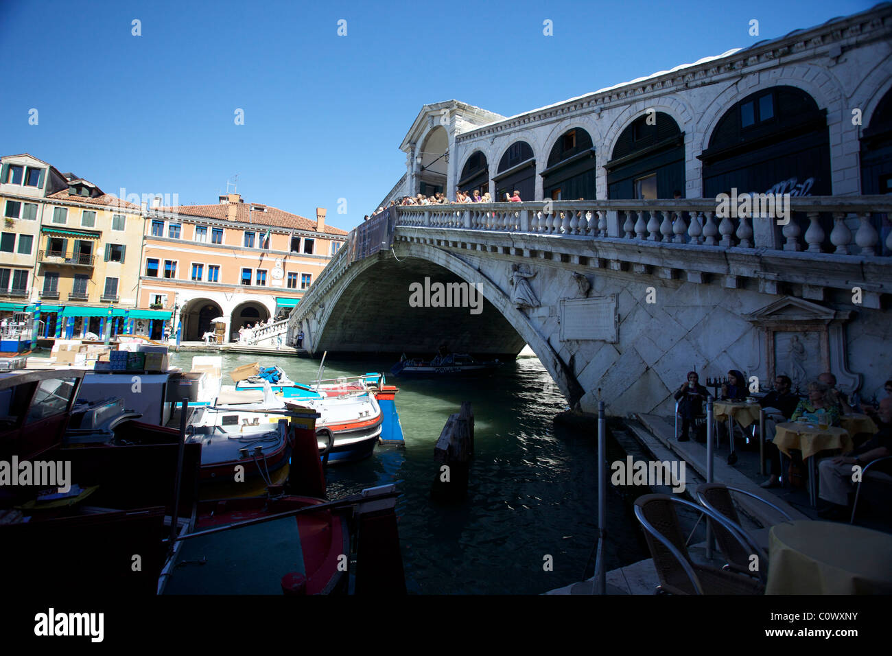 People on the Ponte Rialto bridge in Venice with working boats below Stock Photo