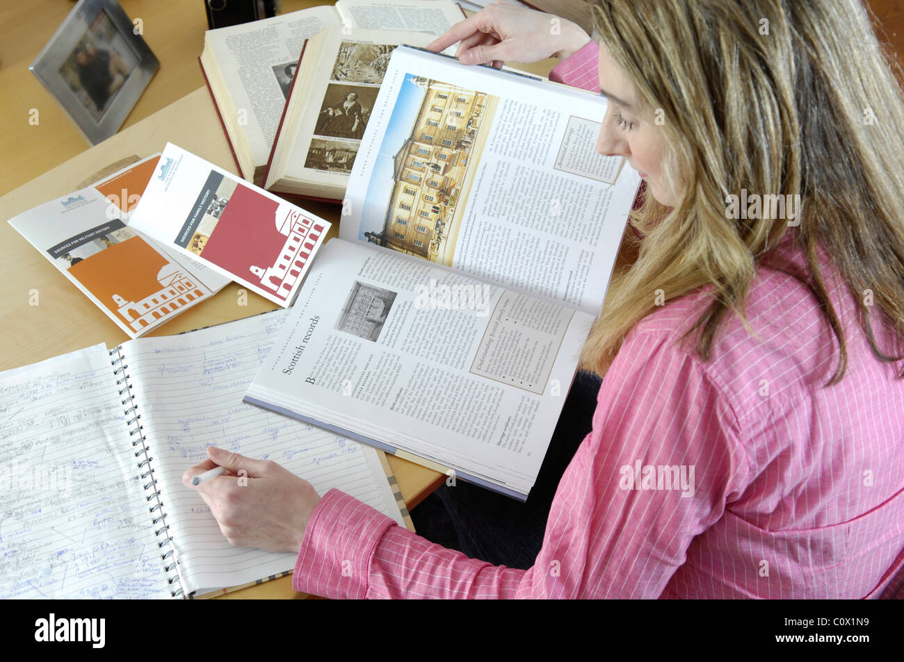 young women researching family history online with books and computer Stock Photo