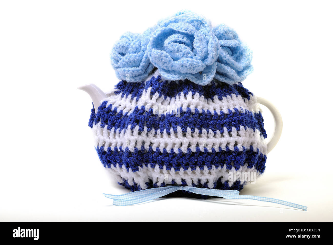 Handmade teacosy  in blue and white with flowers on top all is crocheted with wool and has a gingham blue and white ribbon Stock Photo