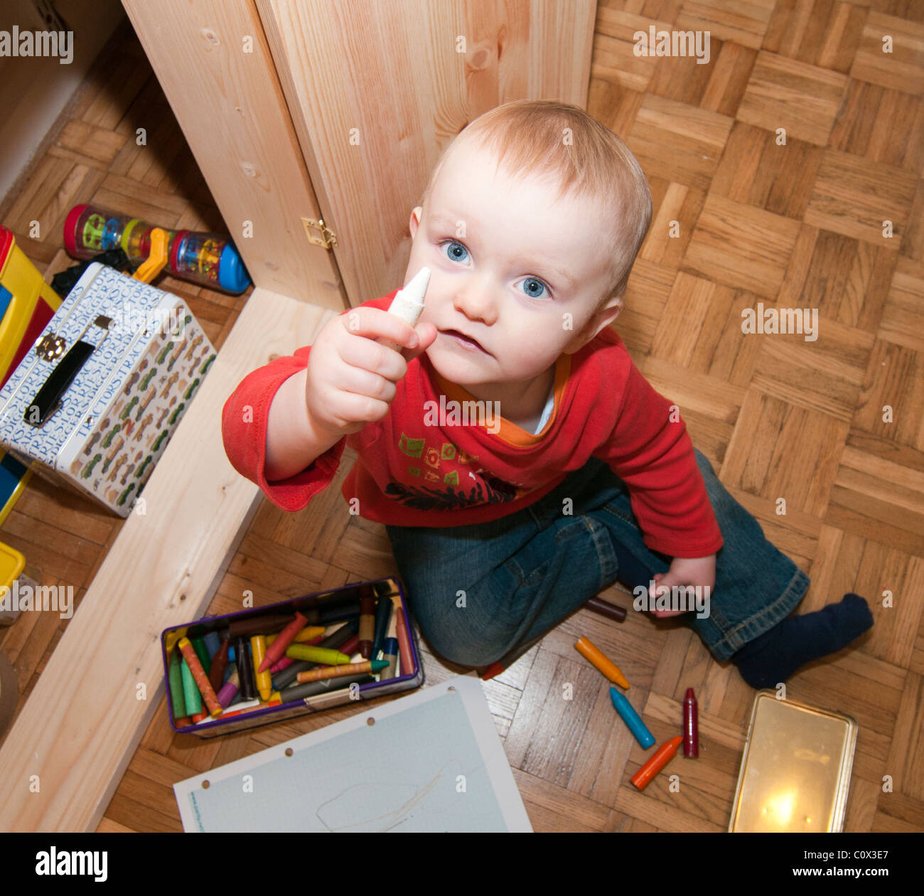Toddler sitting on floor holding a crayon Stock Photo