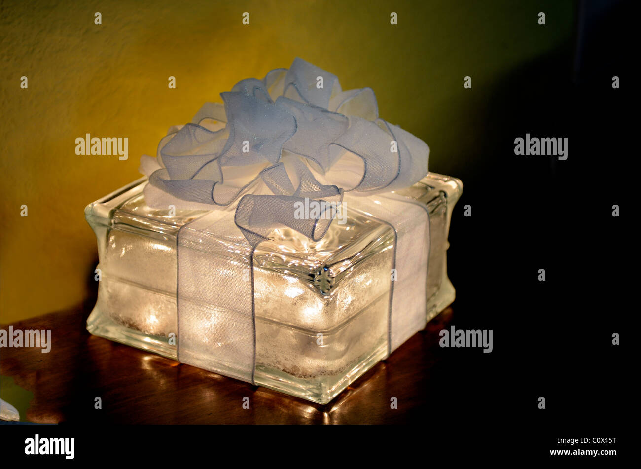 A white glass Christmas decoration box lit from within and topped with a white bow. Stock Photo