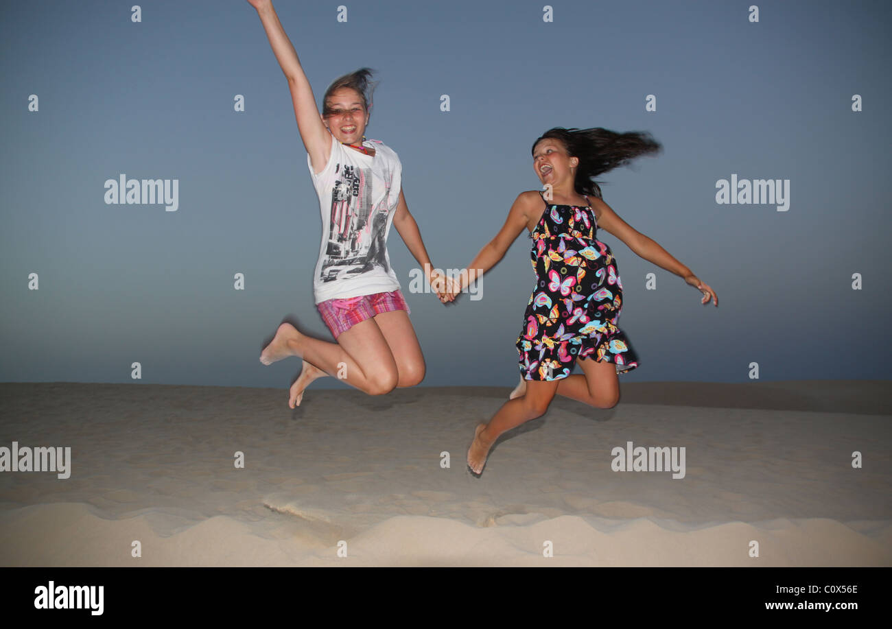 Two girls jumping off sand dune Stock Photo Alamy