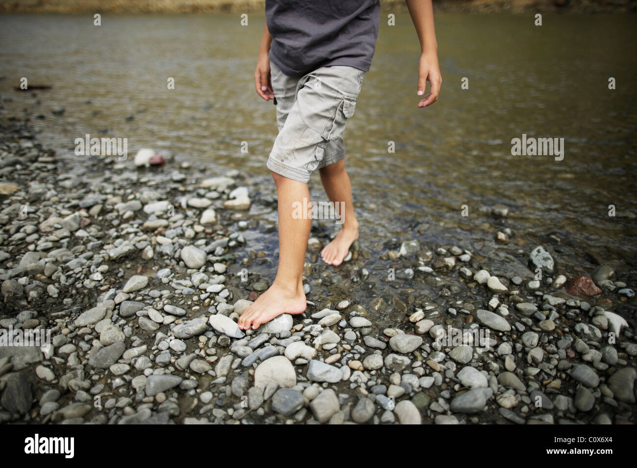 Boy walks barefoot over pebbles, Manawatu river, New Zealand Stock Photo