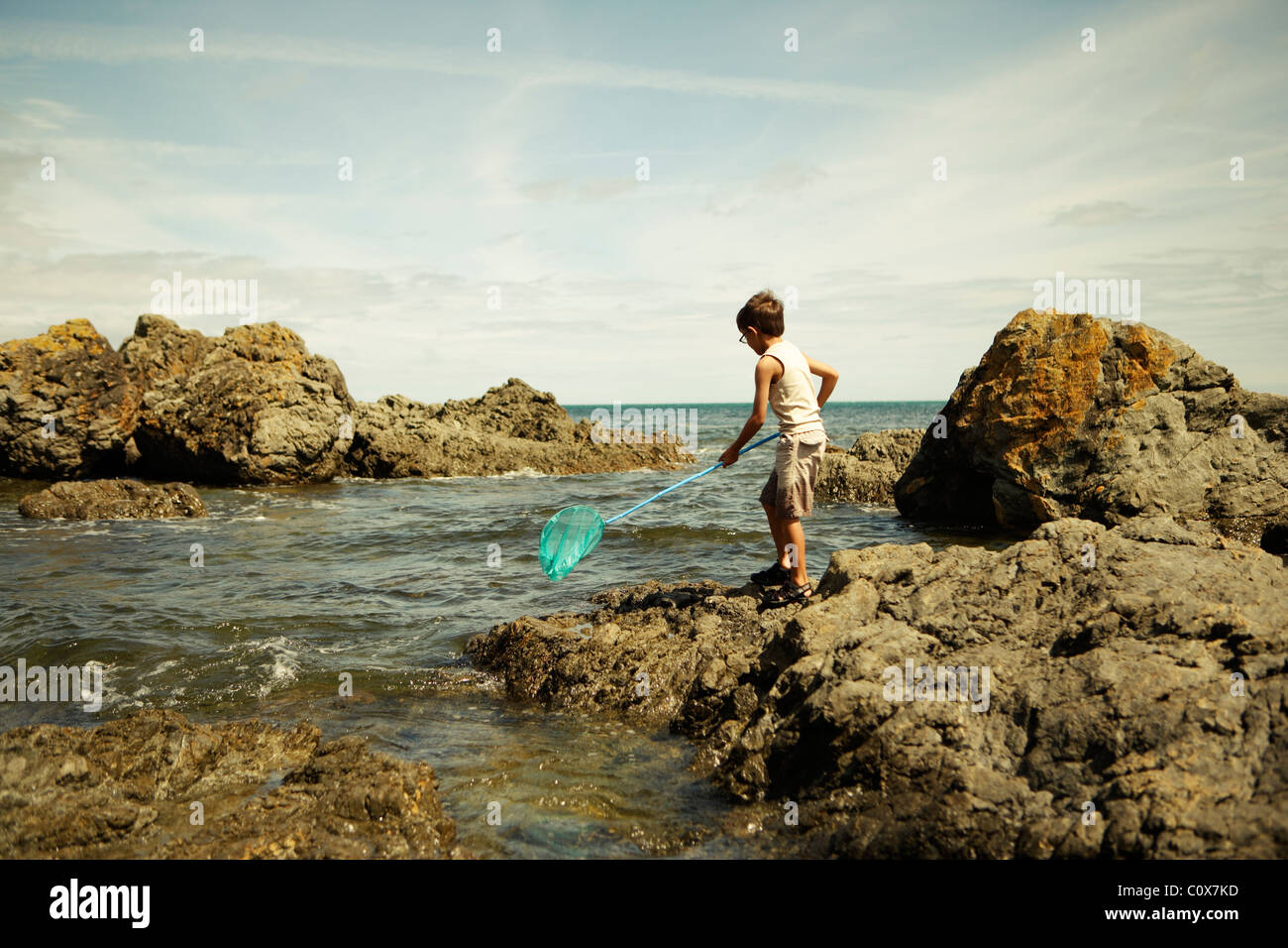 Boy with blue fishing net by the ocean, New Zealand Stock Photo