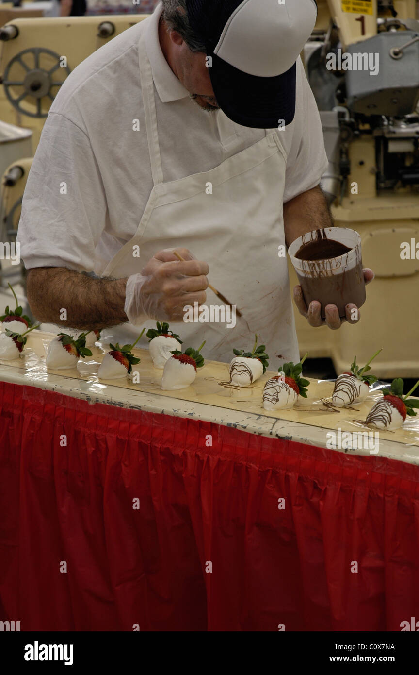 A worker drizzles garnish onto chocolate covered strawberries at the