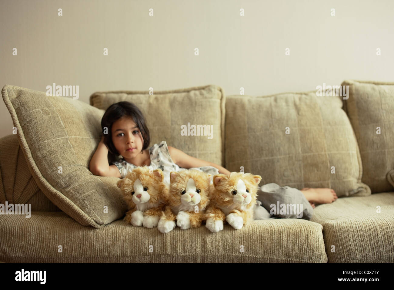 Girl on sofa with three fluffy toy kittens. Stock Photo