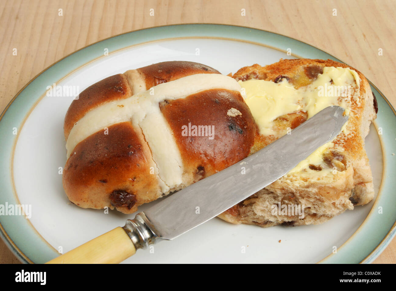 Toasted and buttered hot cross bun with a knife on a plate Stock Photo