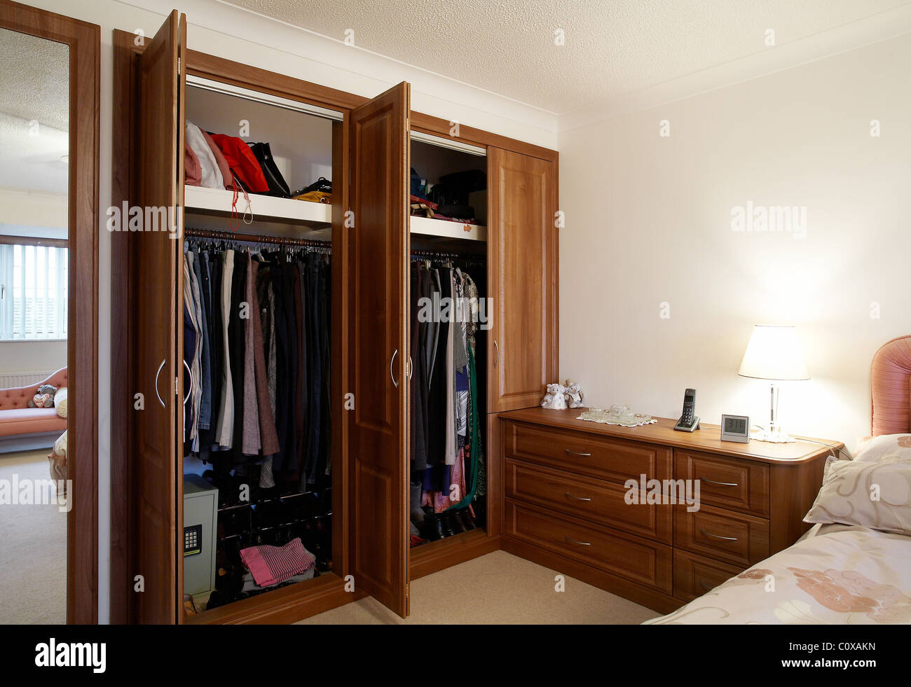 A bedroom with wooden oak wardrobe with doors open in the Uk. Stock Photo