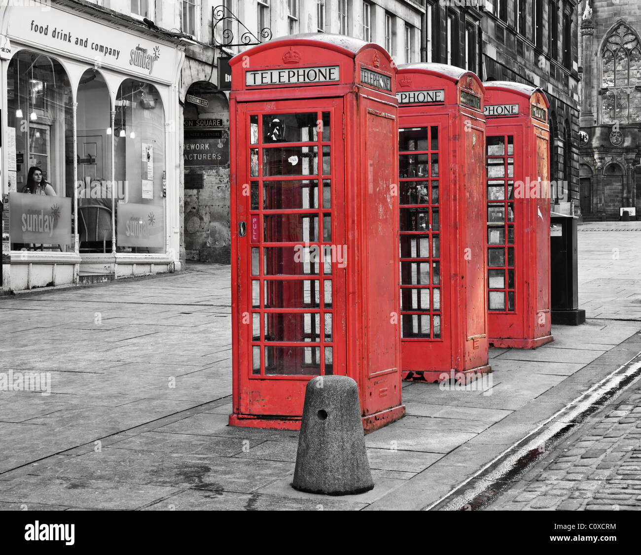 Three red Telephone Boxes on the Royal Mile, Edinburgh, Scotland, UK. A woman is sitting in a cafe window. Stock Photo