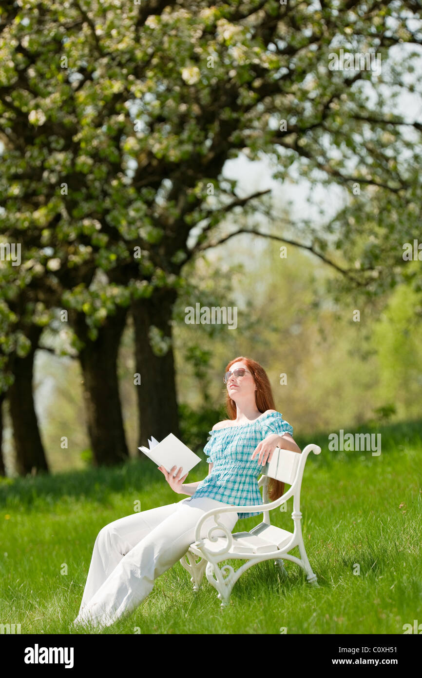 Red hair woman reading book on white bench in a meadow; shallow DOF ...