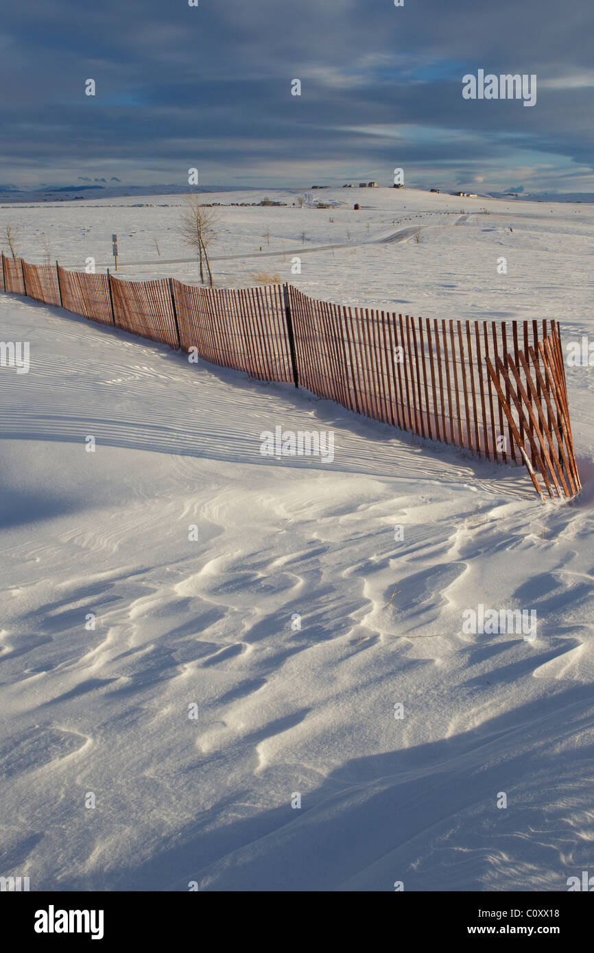 Rough scallops in drifted snow at the end of a fence and smooth drifts behind the snow fence show its impact on wind patterns. Stock Photo