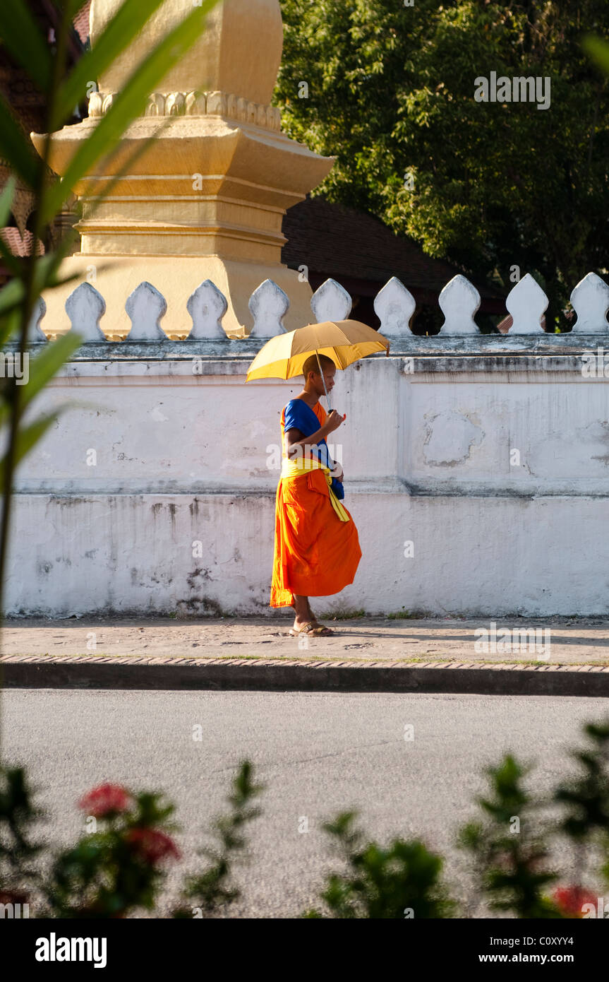 Young monk with an umbrella walking on the street, Luang Prabang, Laos Stock Photo