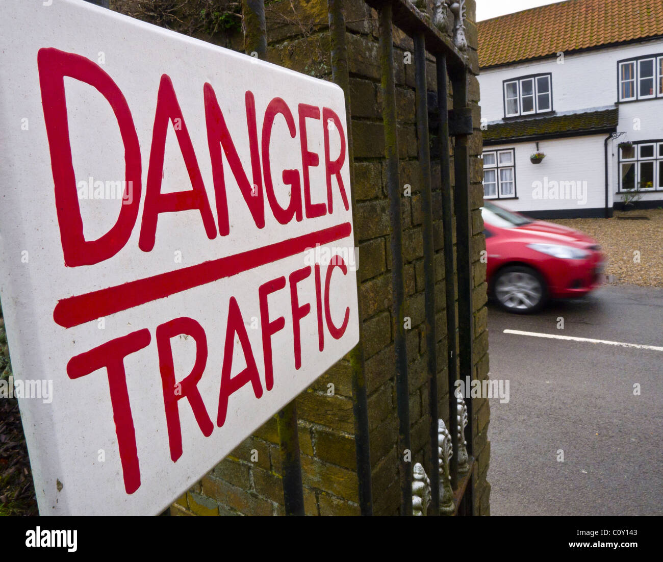 A warning sign reading 'DANGER TRAFFIC'  with a moving car on the road behind Stock Photo