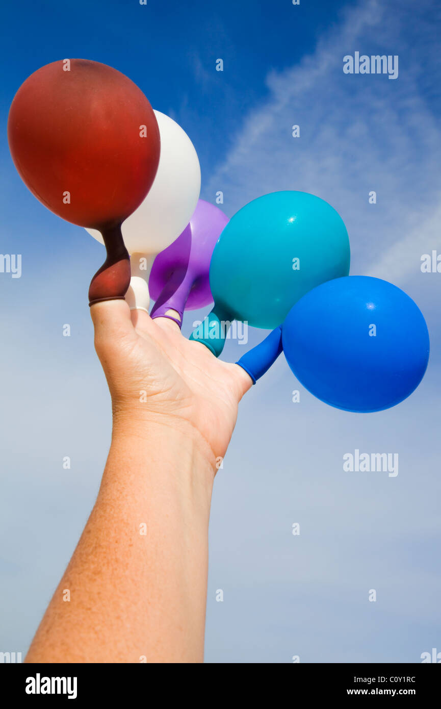 Hand with colored balloons on the fingers against a cloudy blue sky Stock Photo